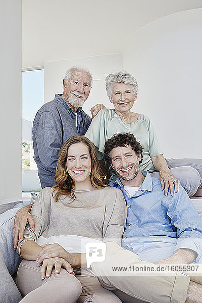 Portrait of happy senior couple with adult children sitting on a couch in a villa