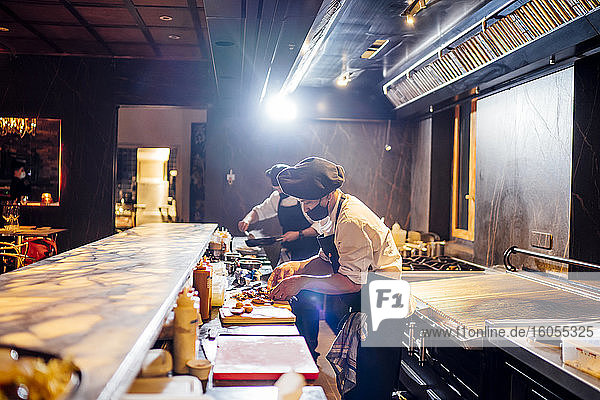 Chefs wearing protective face masks preparing a dish in restaurant kitchen
