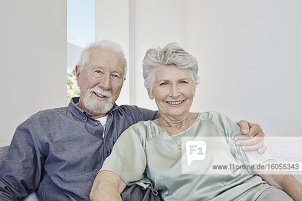 Porträt eines lächelnden älteren Paares  das auf einer Couch in einer Villa sitzt
