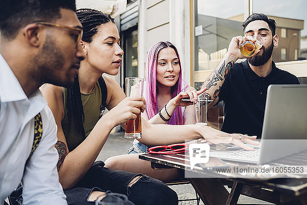 Friends drinking beer and using laptop outdoors at a bar