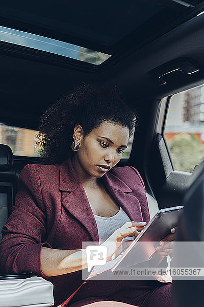 Junge weibliche Berufstätige  die im Auto sitzend ein digitales Tablet benutzt