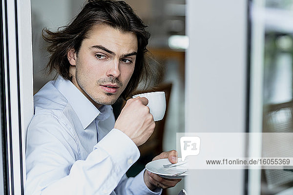 Geschäftsmann hält Kaffeetasse und schaut durch das Fenster  während er in einem Café sitzt