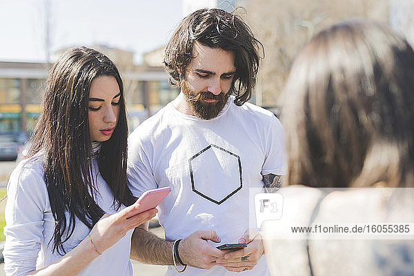 Junge Freunde benutzen Smartphones  während sie mit einer Frau in der Stadt stehen