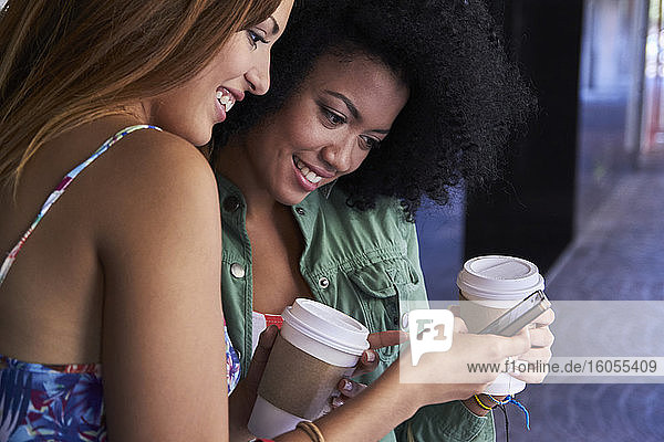 Freundinnen mit Kaffee zum Mitnehmen per Smartphone