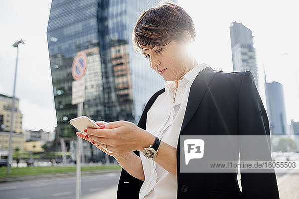 Geschäftsfrau mit kurzen Haaren  die ein Smartphone benutzt  während sie in der Stadt steht