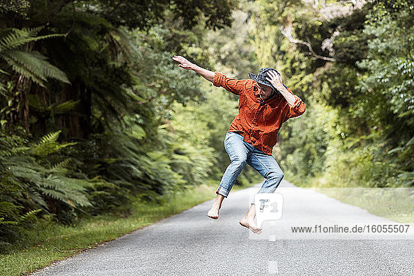 Carefree man jumping on country road amidst trees in forest