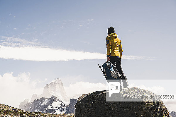 Male hiker holding backpack while standing on rock against sky  Patagonia  Argentina