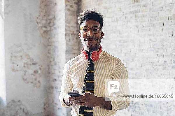 Portrait of smiling young man holding smartphone in loft