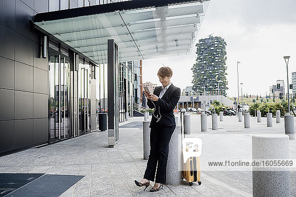 Eine Unternehmerin benutzt ein Smartphone  während sie an einer Säule in der Stadt steht