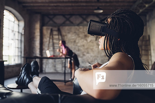 Junge Frau entspannt sich in einem Sessel in einem Loft-Büro und trägt eine VR-Brille