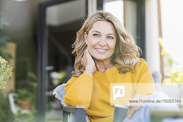 Porträt einer lächelnden reifen Frau  die mit einem digitalen Tablet auf einer Terrasse sitzt und in die Ferne schaut