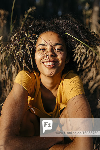 Nahaufnahme einer lächelnden jungen Frau mit Afro-Haar  die im Wald sitzt