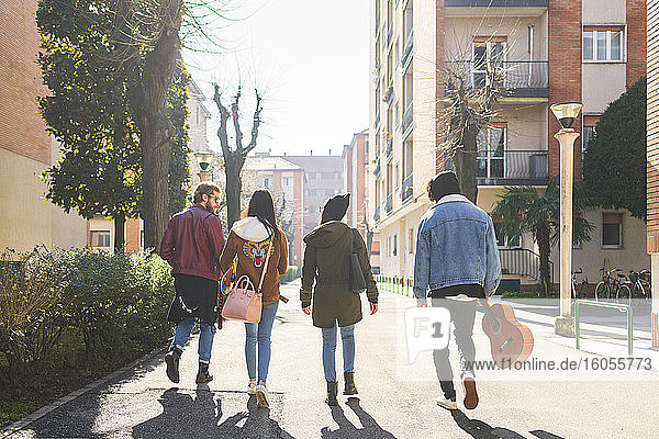 Friends walking on road amidst buildings in city on sunny day