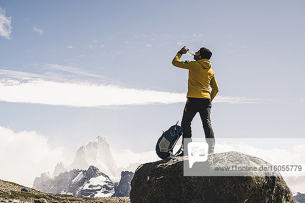 Male hiker drinking water while standing on rock against sky  Patagonia  Argentina
