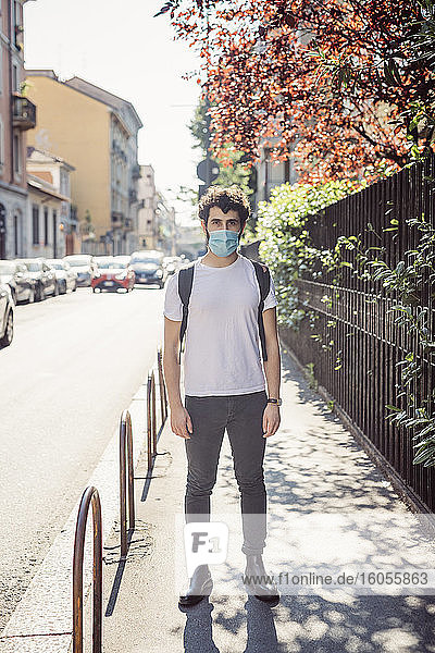 Junger Mann mit Gesichtsmaske auf dem Bürgersteig in der Stadt
