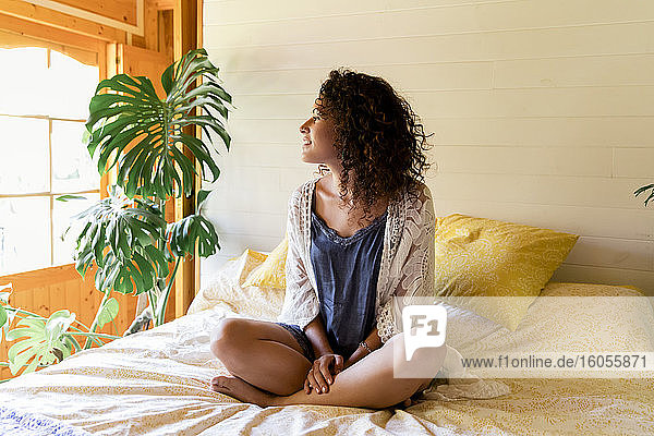 Relaxed young woman sitting on bed in log cabin
