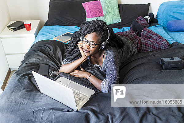 Young woman using laptop watching movie on bed at home