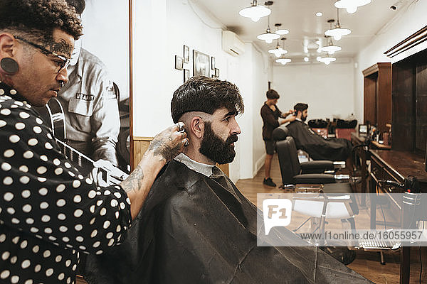 Trendiger Friseur  der die Haare eines Kunden im Salon stylt