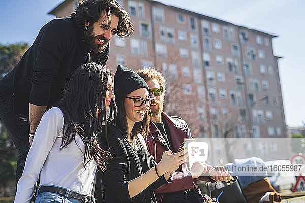 Freunde schauen auf das Smartphone einer jungen Frau in der Stadt