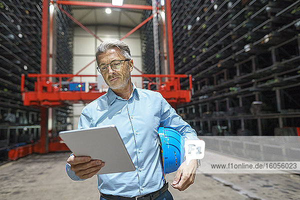 Reifer Geschäftsmann mit Tablet in einem Hochregallager einer Fabrik