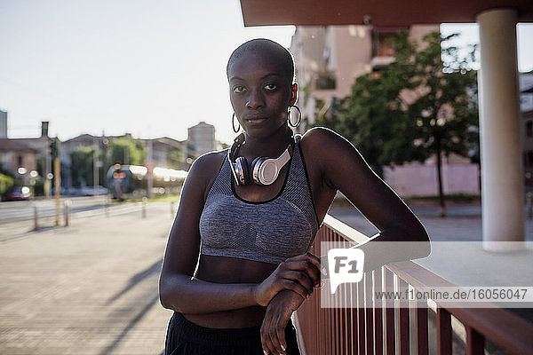 Selbstbewusste junge Frau mit rasiertem Kopf an einem Geländer in der Stadt