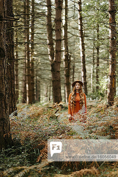 Junge Frau mit langen Haaren und Hut steht inmitten von Pflanzen im Wald