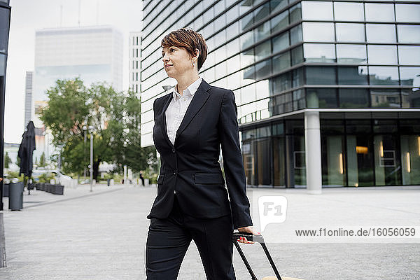 Female entrepreneur with suitcase walking on street against modern building in city
