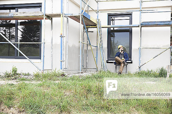 Bauarbeiter  der mit seinem Handy spricht  während er an einem Haus sitzt