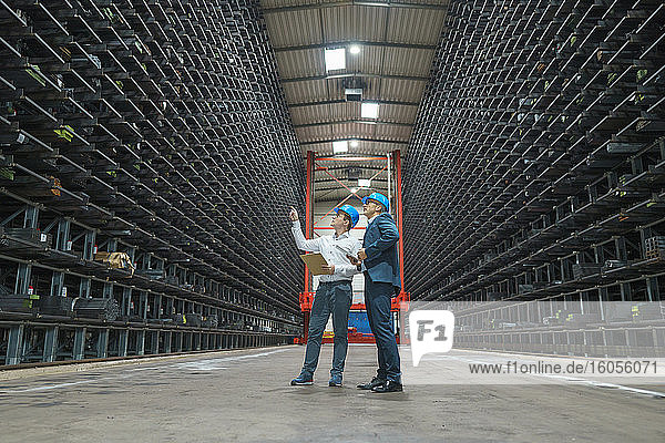 Two businessmen having a meeting in a high rack warehouse of a factory
