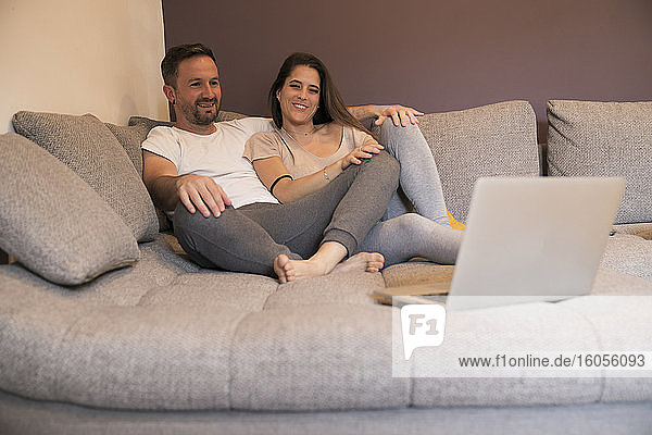 Couple watching movie over laptop while relaxing on sofa at home