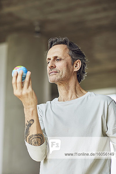 Älterer Mann hält Mini-Globus in einer Dachgeschosswohnung