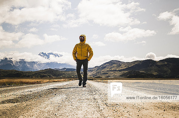 Männlicher Wanderer mit den Händen in den Taschen  der auf einer unbefestigten Straße im Torres Del Paine National Park  Patagonien  Chile  wandert