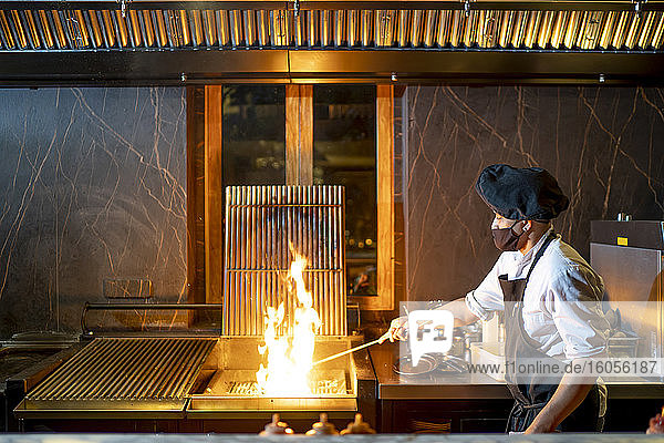 Chef wearing protective face mask preparing grill in restaurant kitchen