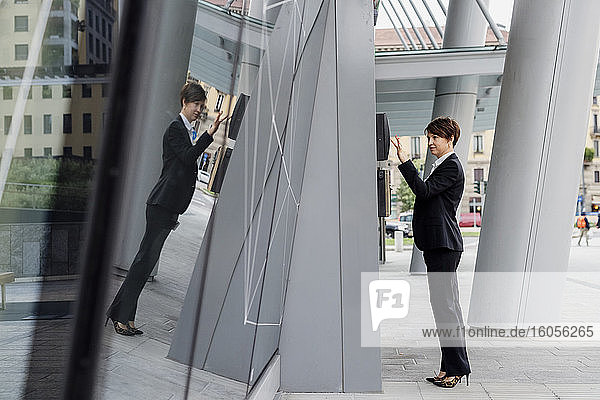Geschäftsfrau mit kurzen Haaren  die einen Geldautomaten benutzt  während sie über ein modernes Gebäude in der Stadt nachdenkt