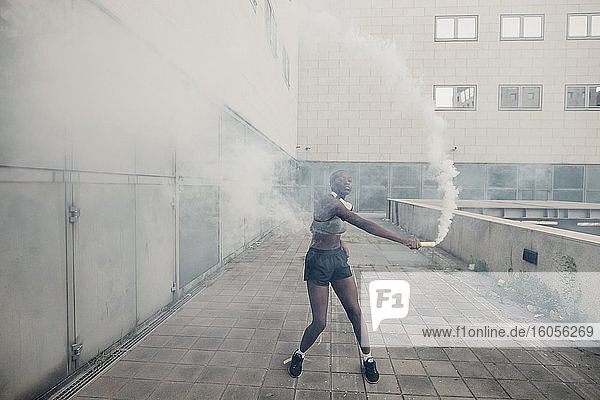 Junge Frau spielt mit einer Rauchbombe  während sie auf dem Fußweg vor einem Gebäude in der Stadt steht