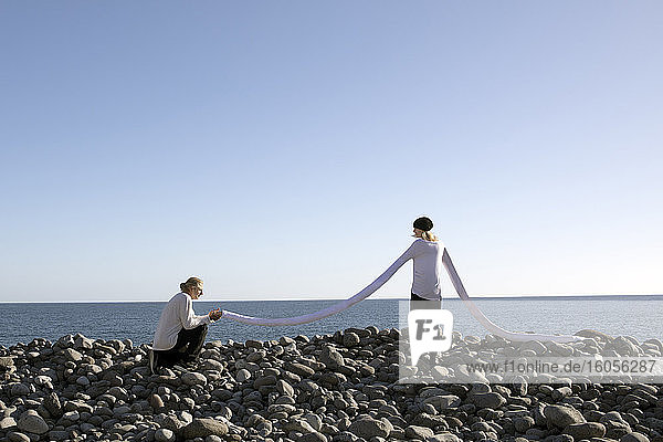 Mann macht ihr einen Heiratsantrag  während er die lange künstliche Hand der Frau am Strand gegen den klaren Himmel hält