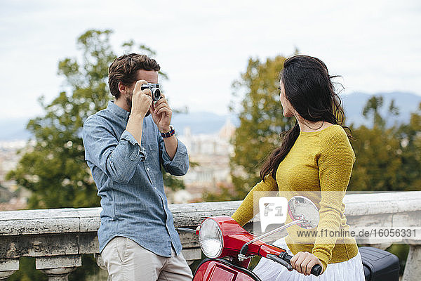 Junger Mann fotografiert Freundin auf Vespa sitzend