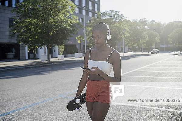 Junge Frau hört Musik über Kopfhörer und benutzt ein Mobiltelefon  während sie auf der Straße geht