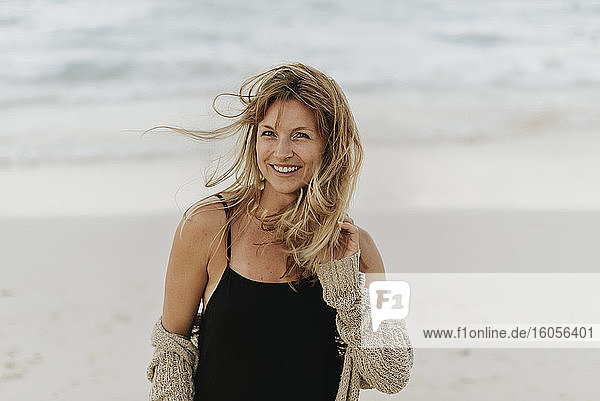 Porträt einer lächelnden erwachsenen Frau mit blondem Haar  die am Meer steht