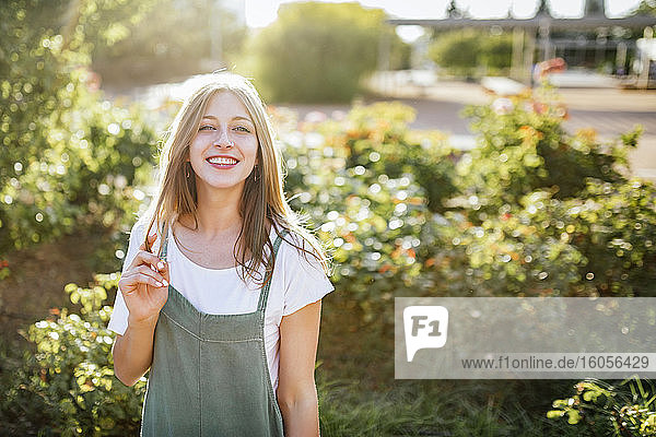 Porträt einer lächelnden jungen Frau im öffentlichen Garten bei Gegenlicht