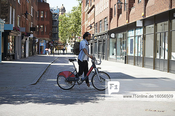 Young man crossing the street with rental bike  London  UK