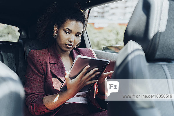 Junge Unternehmerin  die im Auto sitzend ein digitales Tablet benutzt