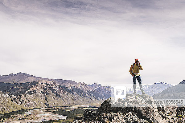 Mature man talking over smart phone while standing on rock against sky  Patagonia  Argentina