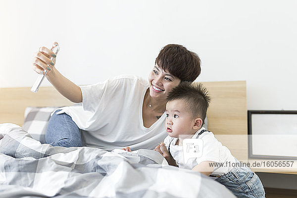 Lächelnde Mutter nimmt Selfie mit niedlichen Sohn auf Bett zu Hause