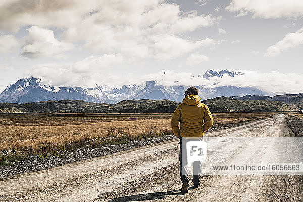 Älterer Mann  der auf einer unbefestigten Straße gegen den bewölkten Himmel läuft  Torres Del Paine National Park  Patagonien  Chile