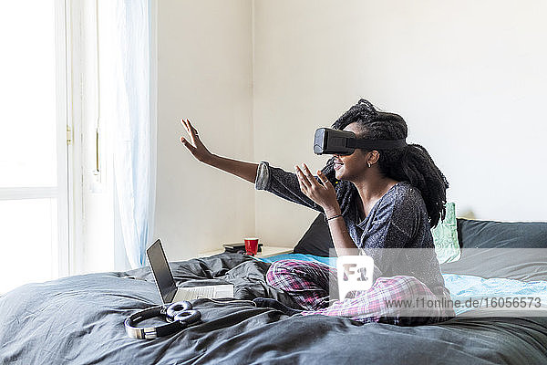 Junge Frau mit Virtual-Reality-Brille auf dem Bett sitzend