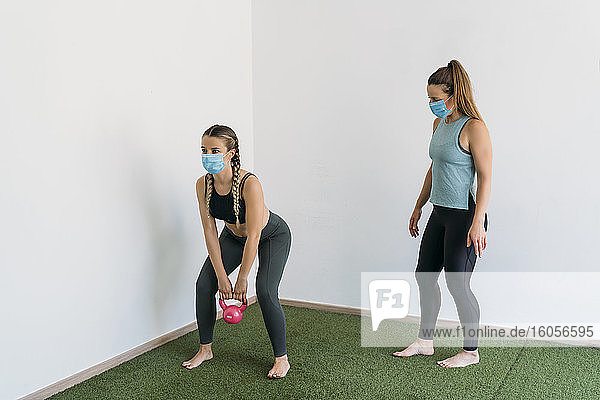 Frau mit Gesichtsmaske beim Training mit Trainer im Fitnessstudio