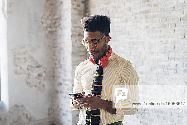 Stilvoller junger Mann  der im Loft sein Smartphone benutzt
