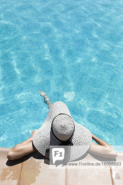 Junge Frau mit Hut  die sich an einem sonnigen Tag im Schwimmbad eines Ferienortes entspannt