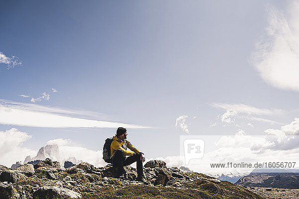 Male hiker sitting on mountain against sky during sunny day  Patagonia  Argentina